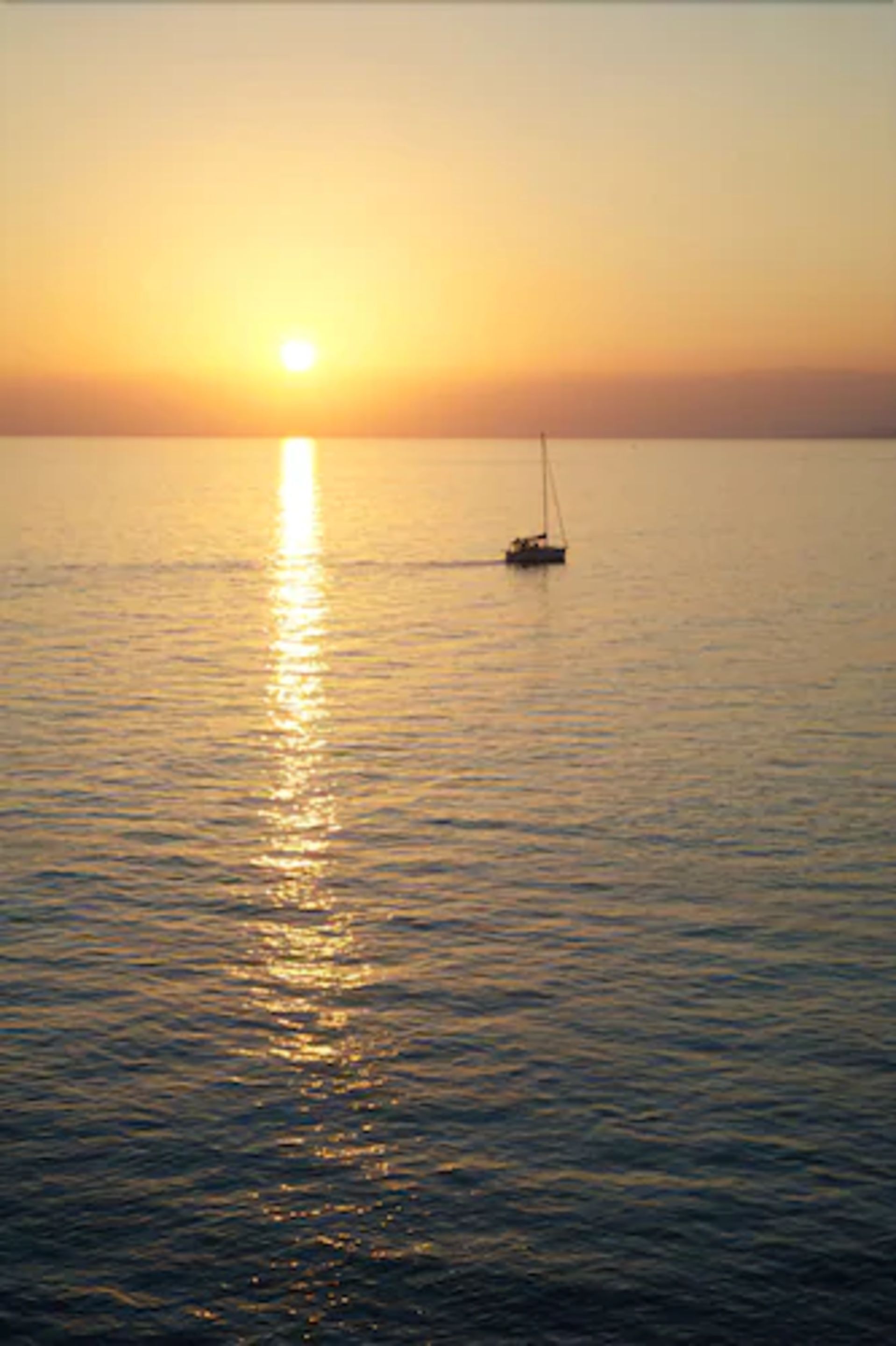 Een rustige zee bij zonsondergang, met een zeilboot in de verte.