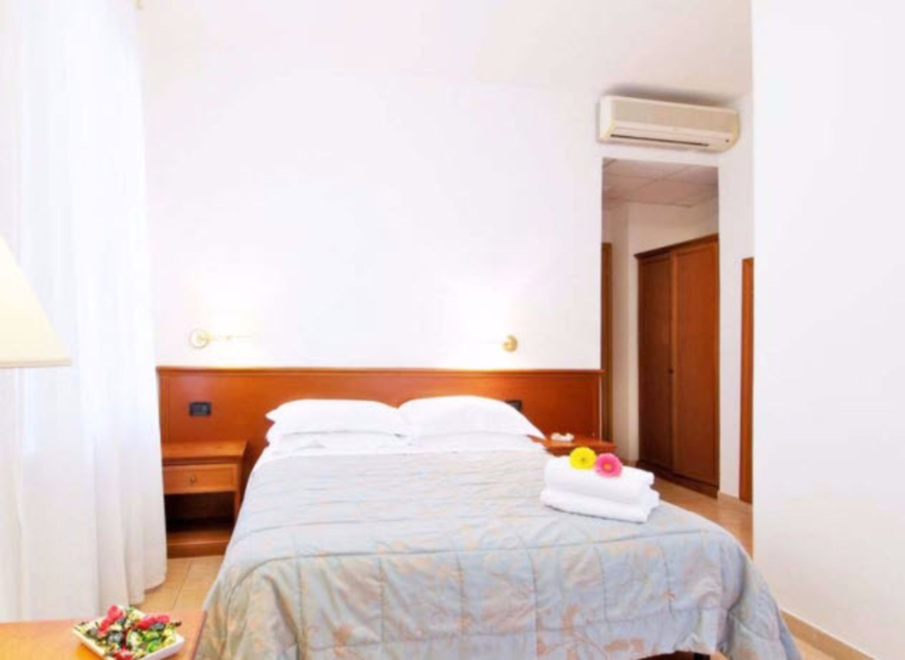 A hotel room with a bed, a nightstand, a lamp, and a small table with a flower arrangement.