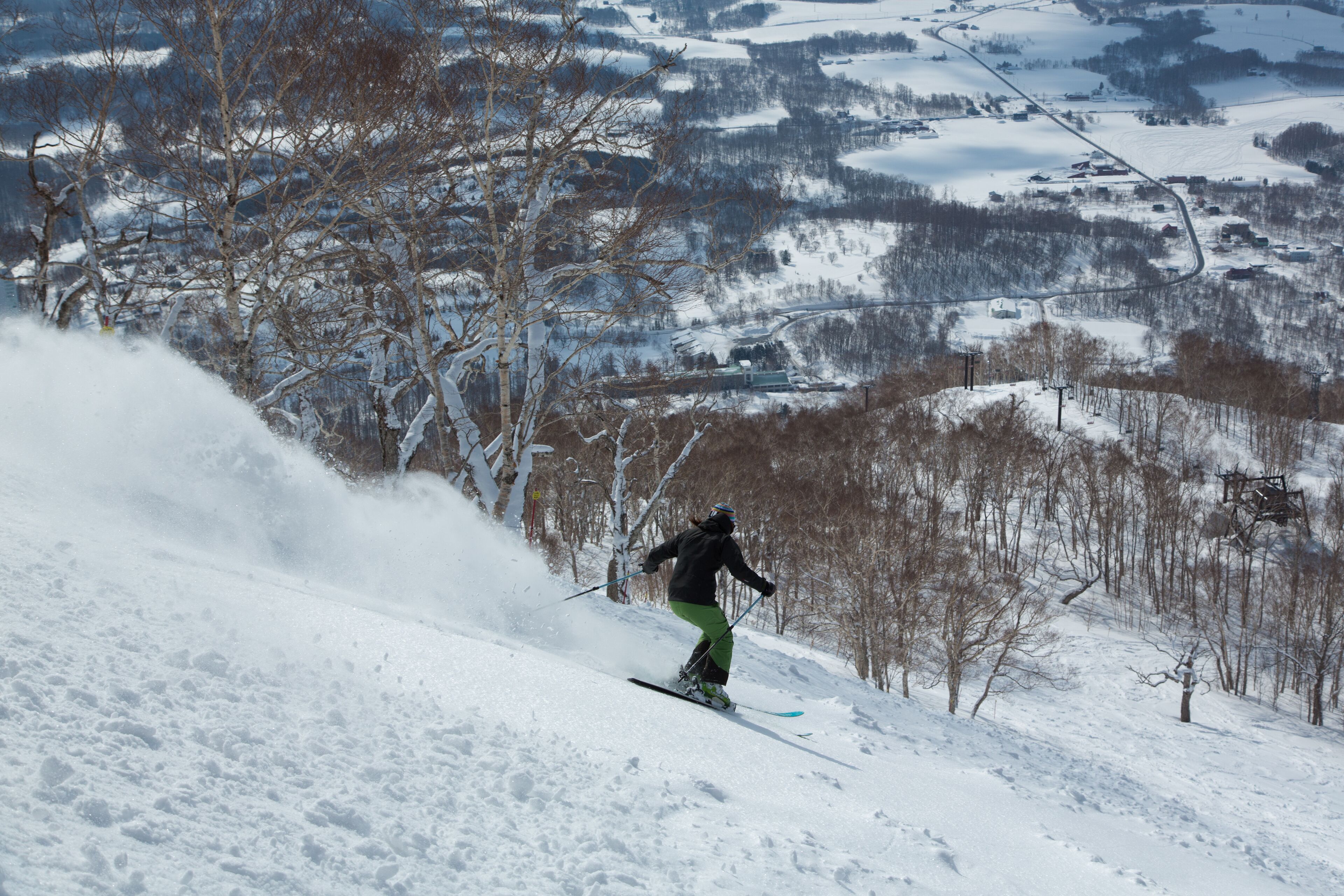 A person skiing down a snowy slope with a view of a village in the background.