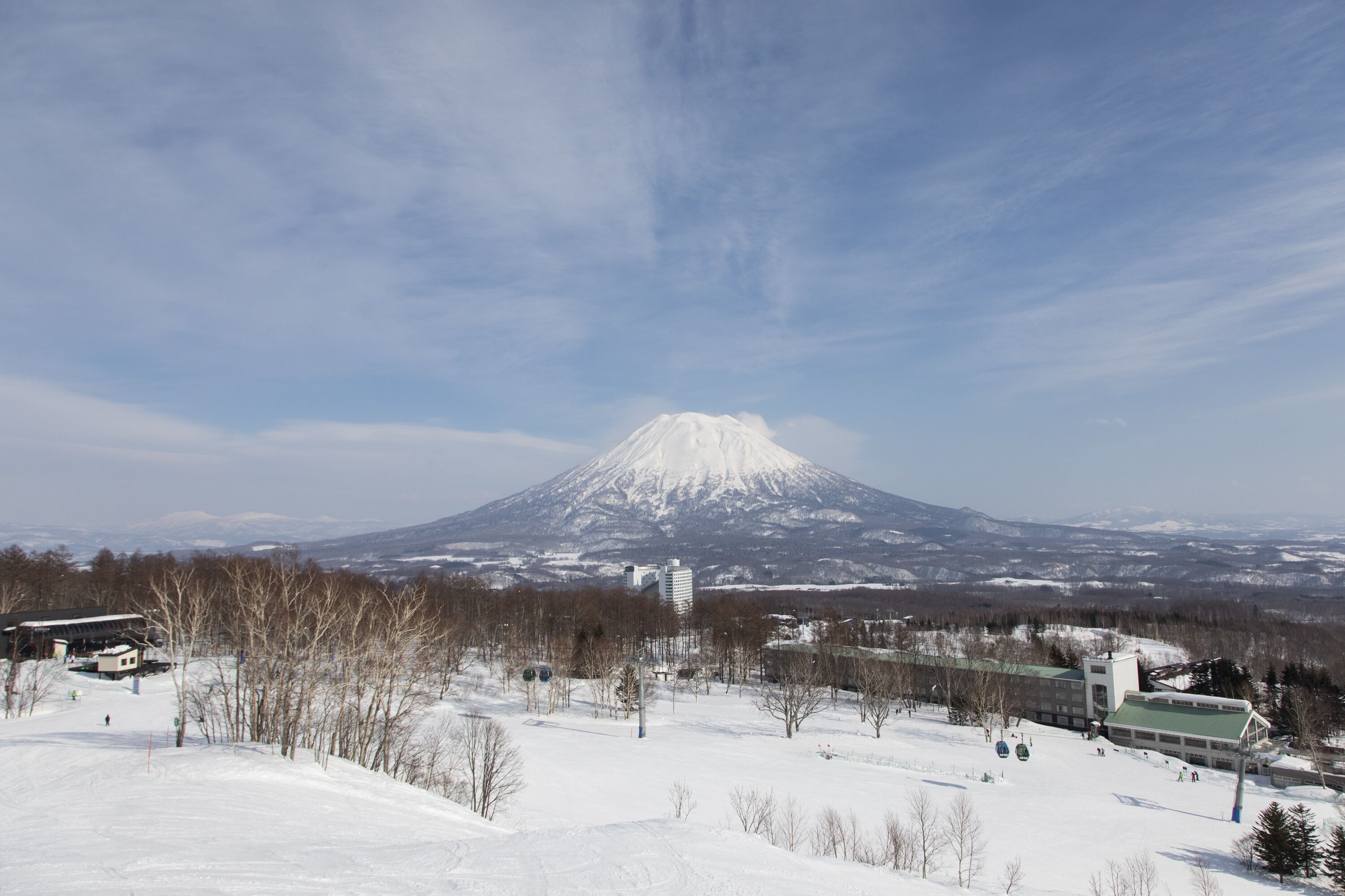 Un paysage enneigé avec une montagne imposante en arrière-plan, qui ressemble probablement à un volcan, et un bâtiment doté d’un toit végétalisé au premier plan.