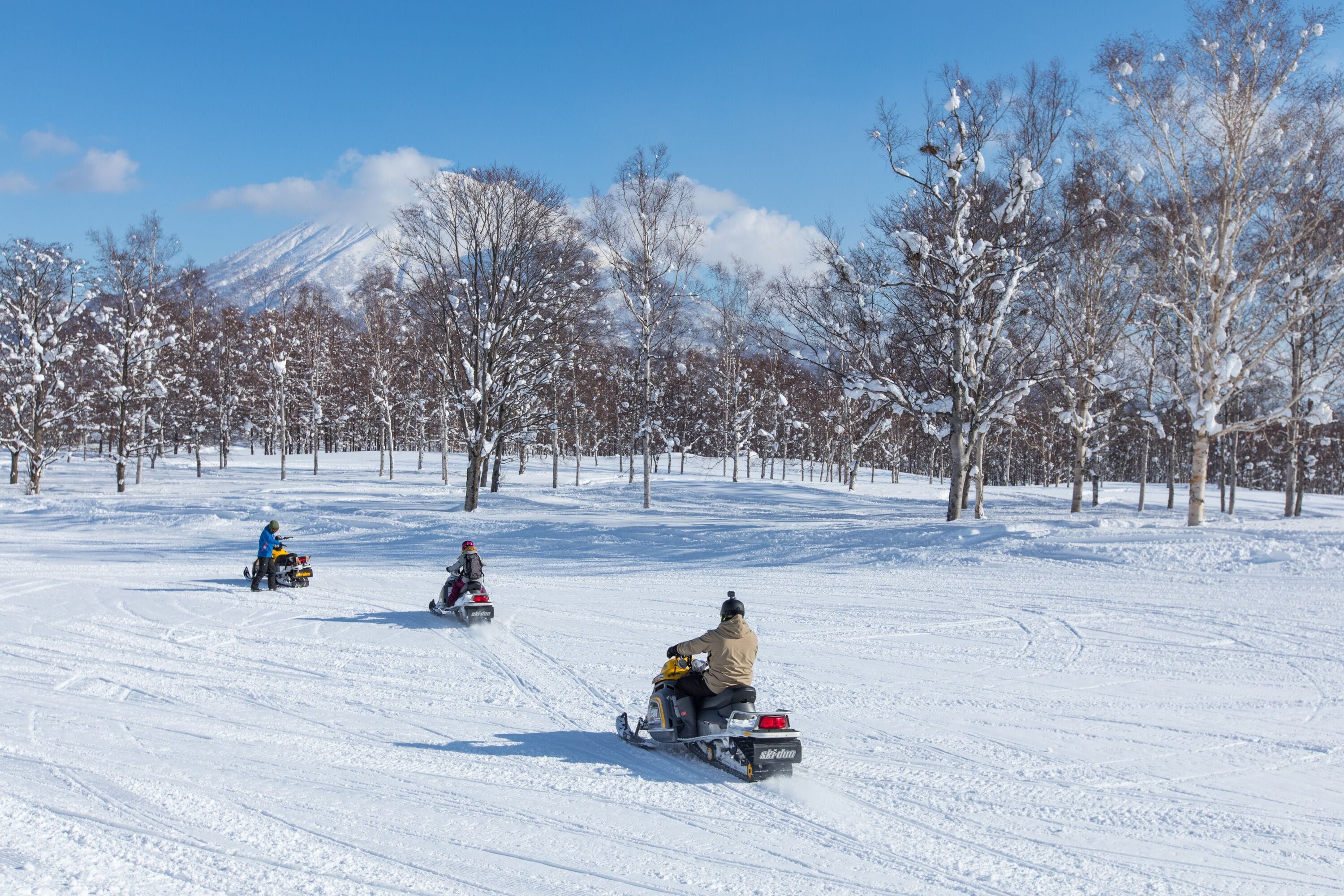 A snowy landscape with three snowmobiles on a trail.