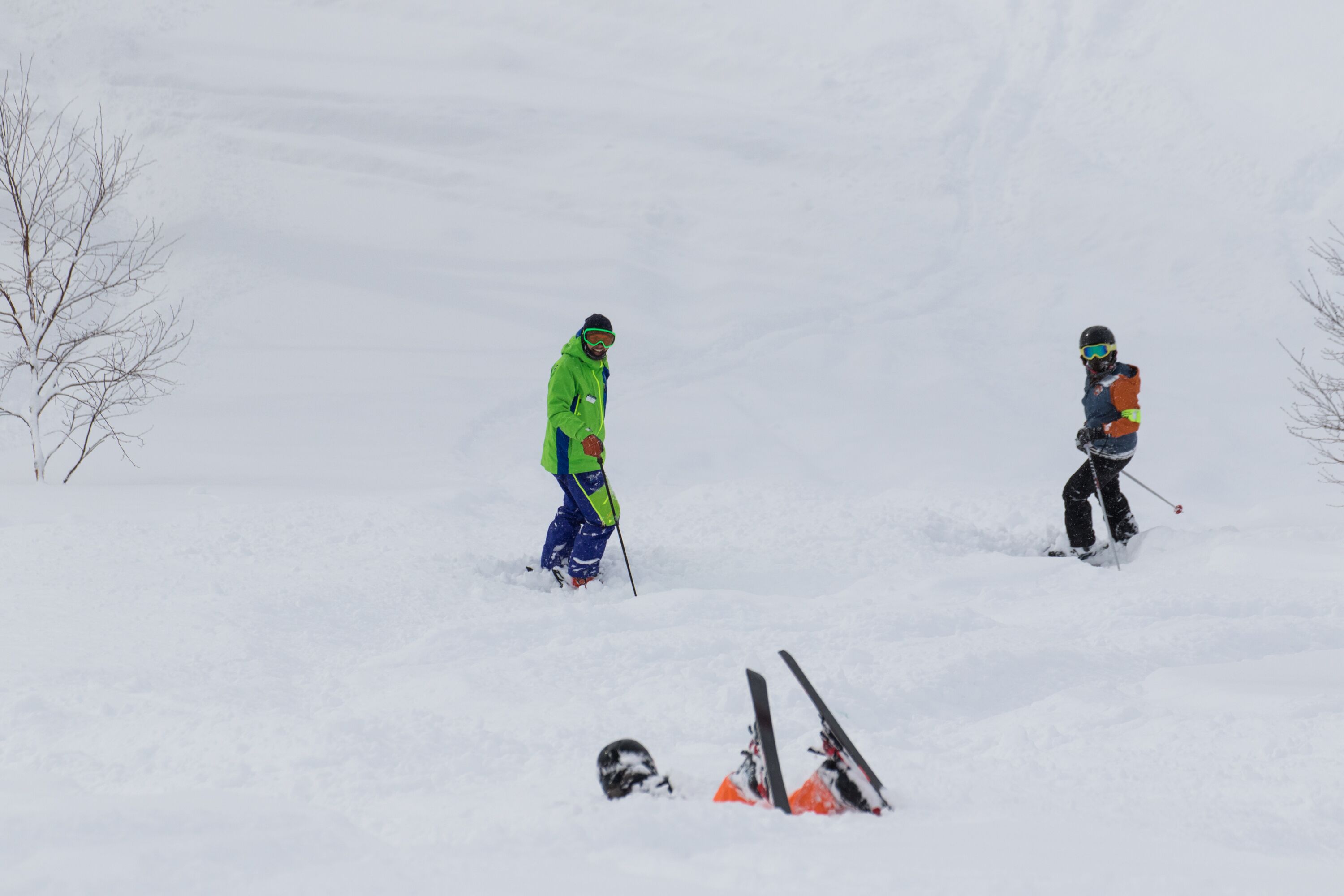 A snowy landscape with two skiers and a pair of skis on the ground.