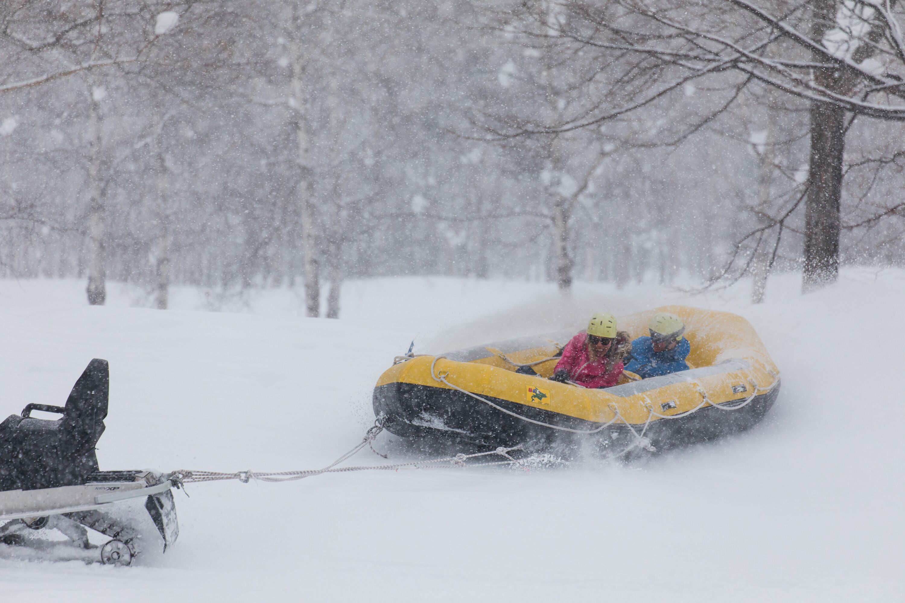 Een besneeerd landschap met een gele sneeuwscooter en een persoon in een roze jas.