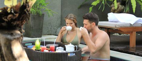 A couple relaxing in a pool with a wicker tray containing food and drinks.