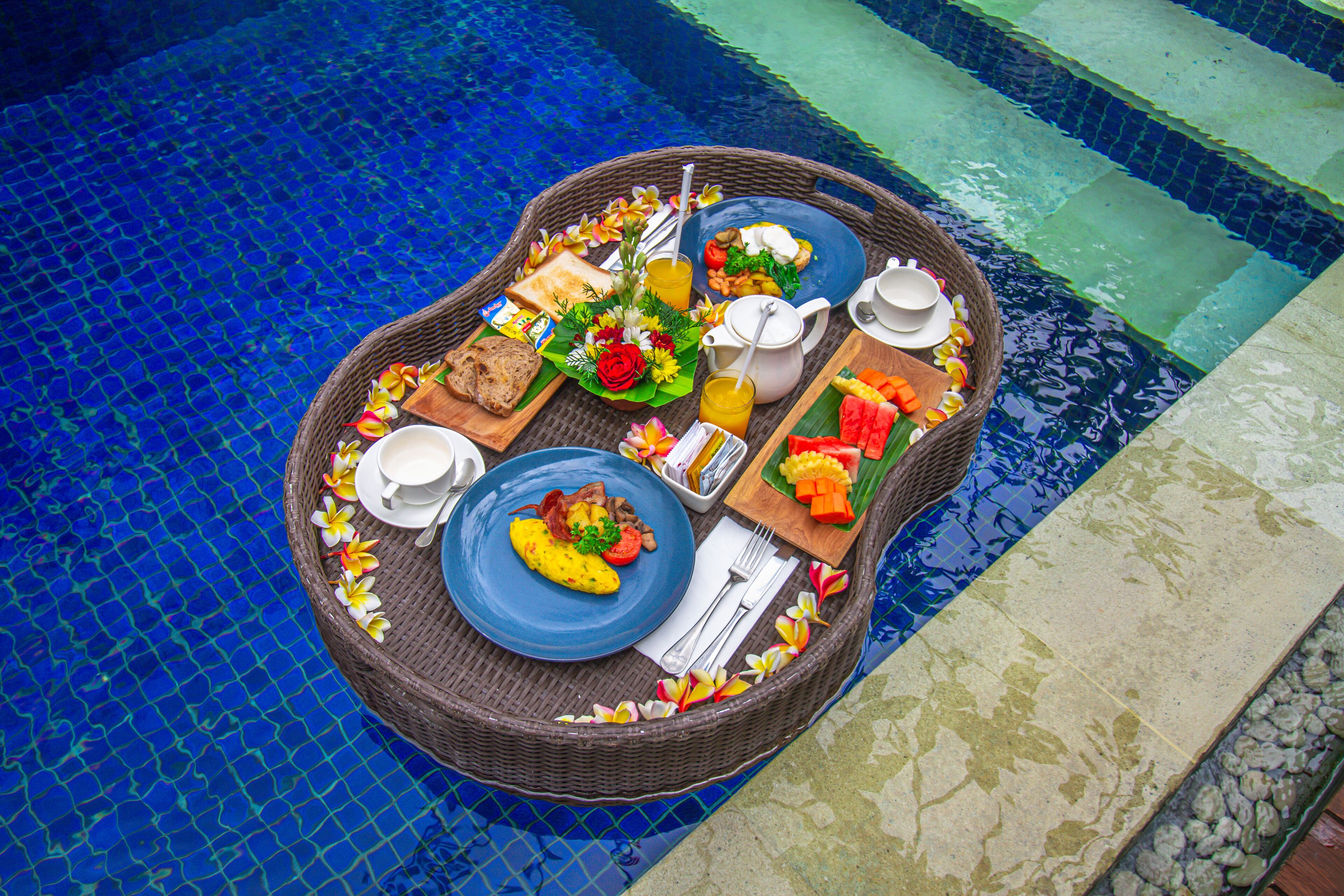 Montaje de un bufé de desayuno en una mesa junto a la piscina, con diversas opciones de comida y bebidas.