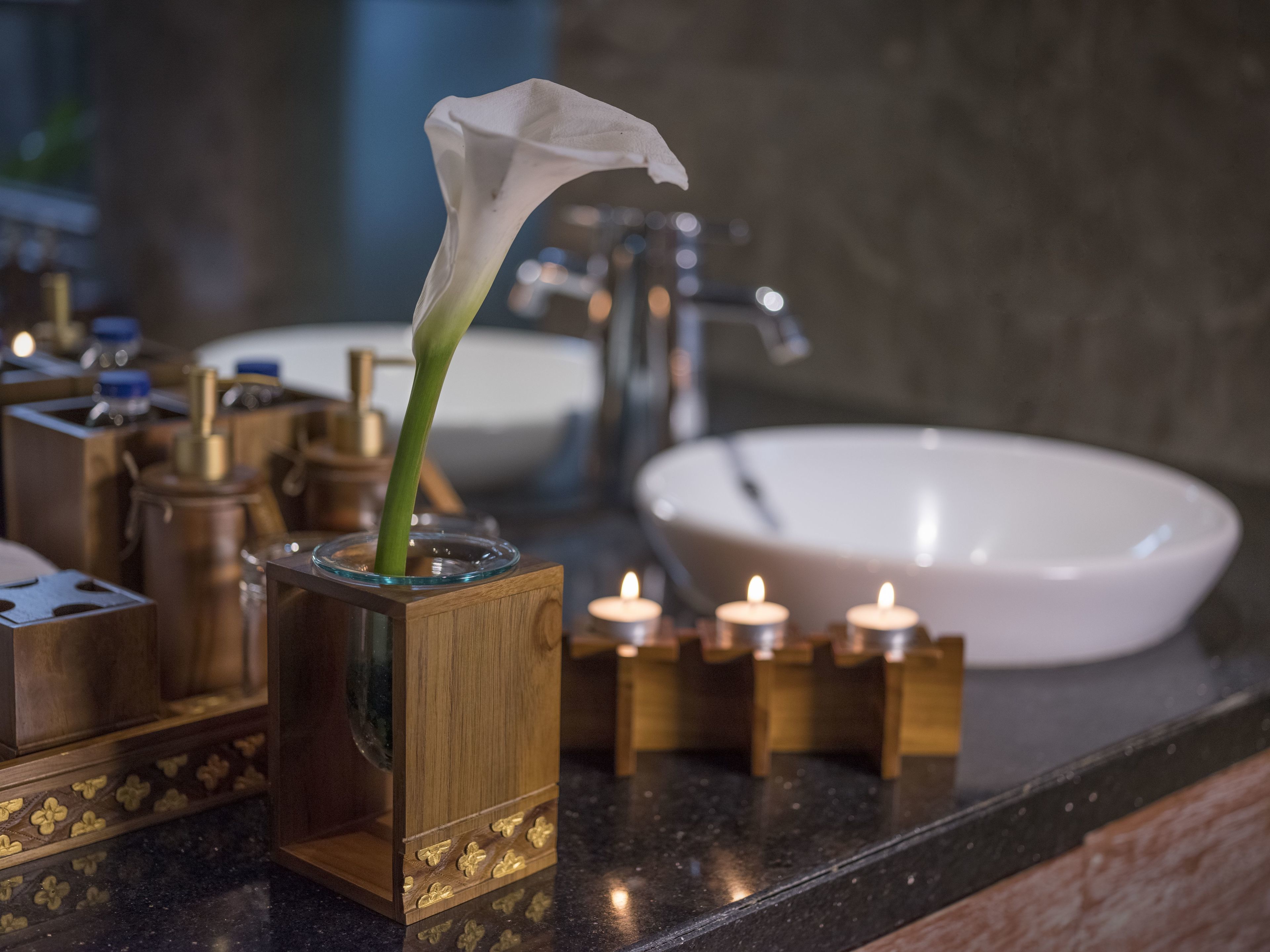 A bathroom vanity with a white sink, a glass vase with a white flower, and candles on the counter.