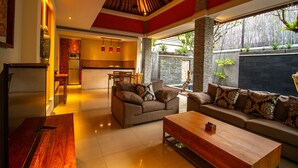 A modern living room with a sofa, coffee table, and a dining area with a table and chairs. - The Wolas Villa & Spa (Seminyak)