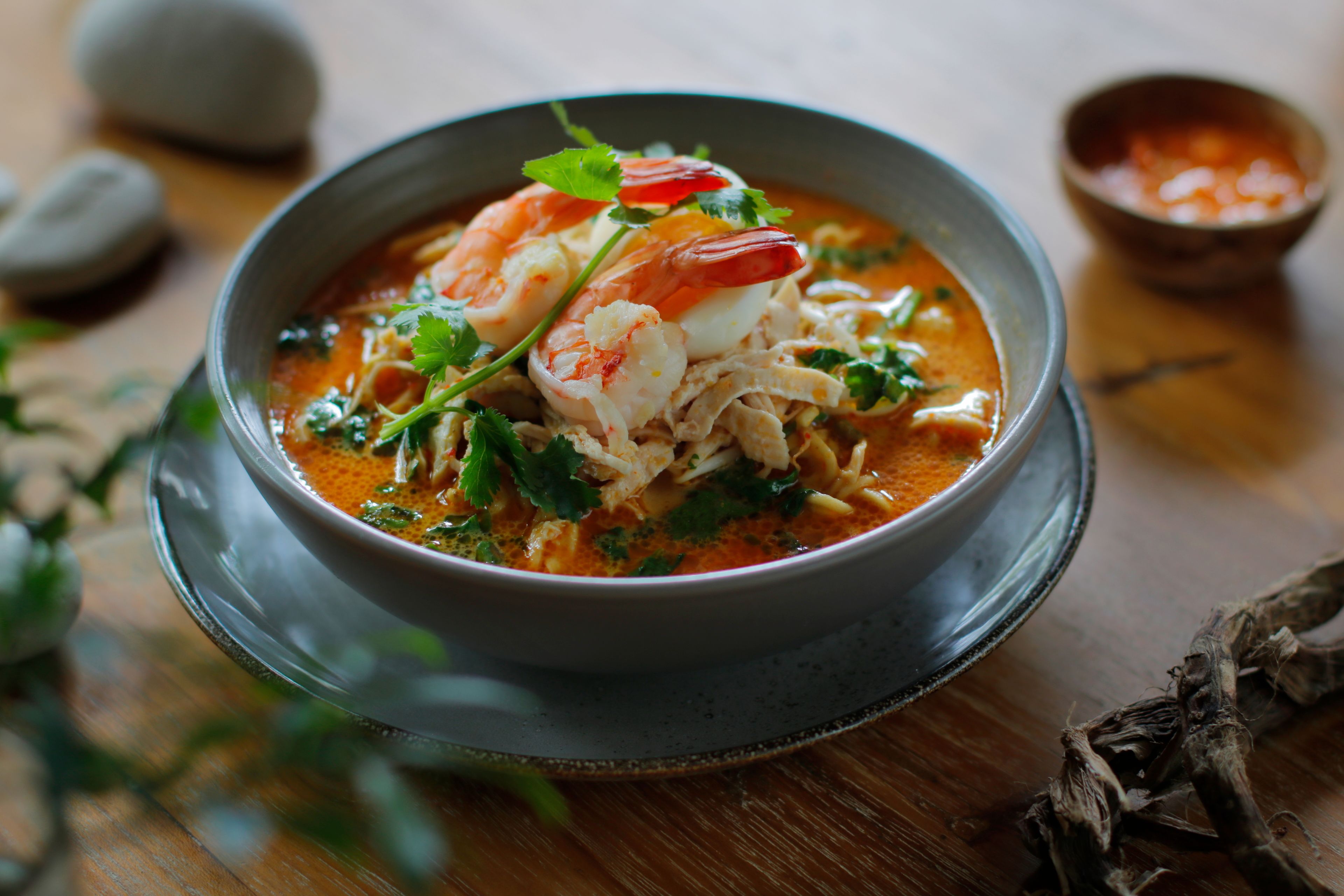 A bowl of soup with shrimp and herbs, served on a ceramic plate.