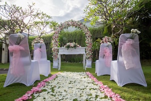 Decoração de casamento ao ar livre com cadeiras brancas e um arco de flores.