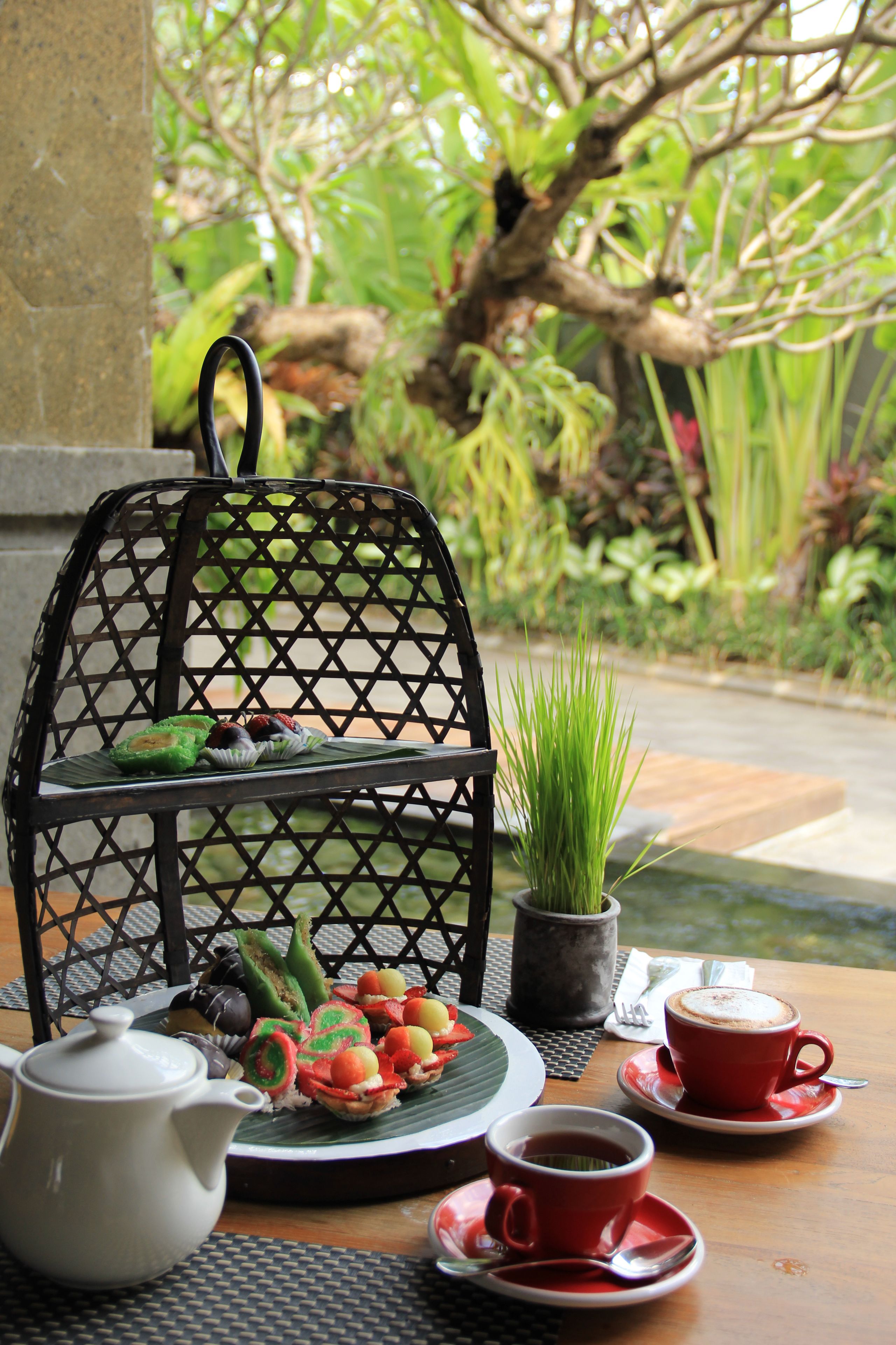 A table set with a teapot, cups, a tray with snacks, and a decorative metal stand.