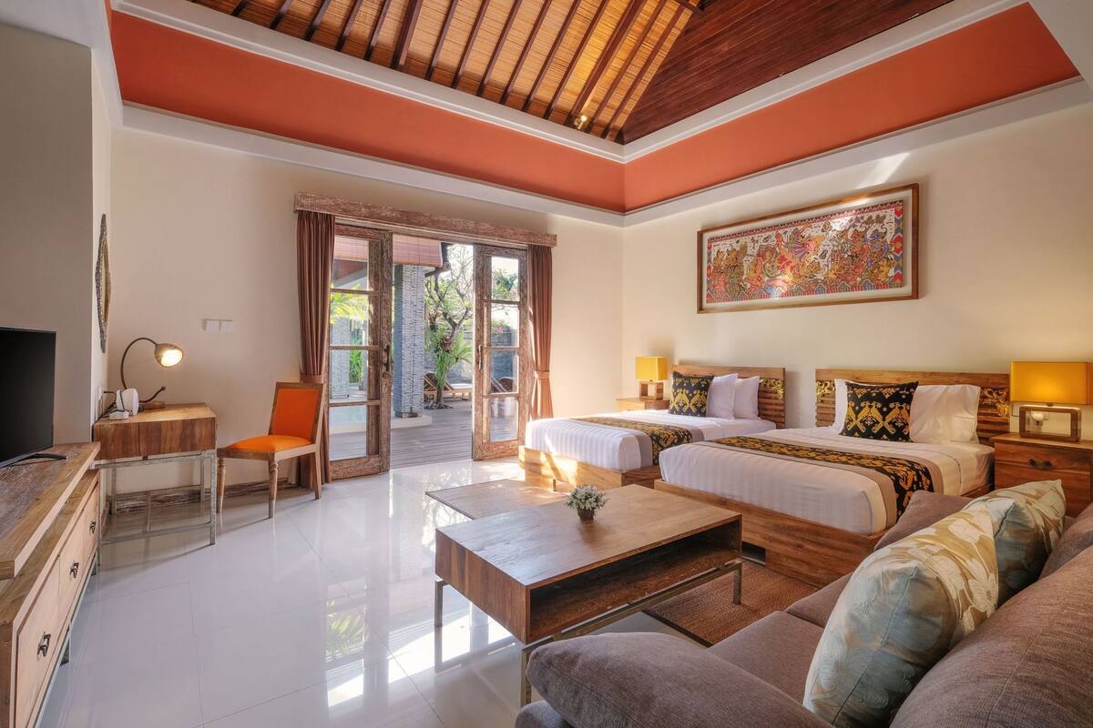 Quarto de hotel com duas camas, um sofá, uma televisão, uma escrivaninha e uma janela grande.