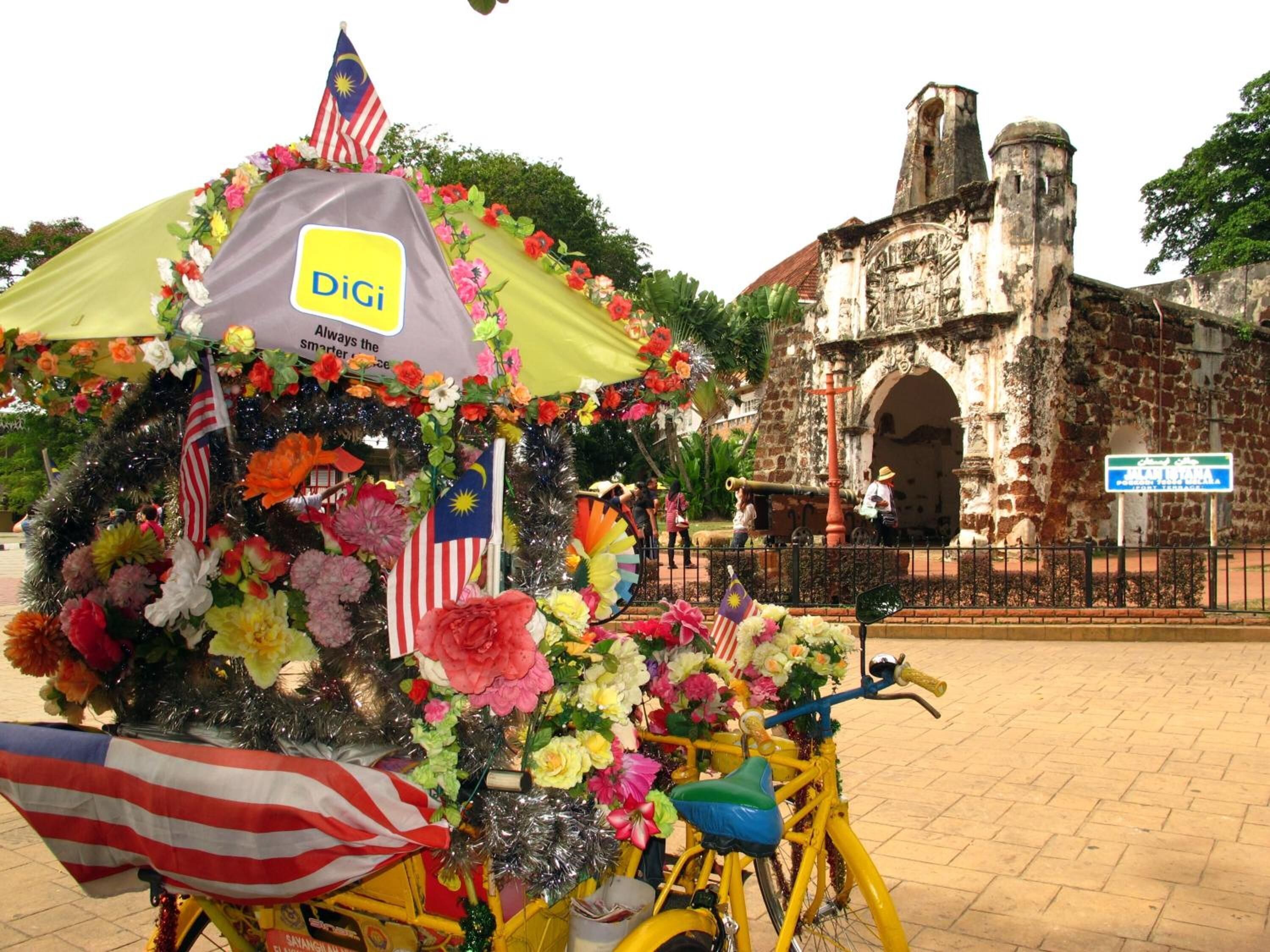 Un vélo jaune, orné de fleurs et de drapeaux, est garé devant un bâtiment historique en pierre, sur lequel on peut voir une enseigne.
