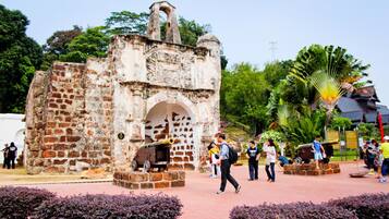 Una antigua estructura de piedra con una entrada en arco y un cañón, rodeada de vegetación y personas.