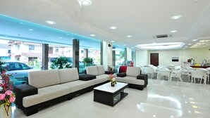 A modern hotel lobby with a large sectional sofa, a coffee table, and a dining area with white chairs. - Hallmark View Hotel (Malacca City)