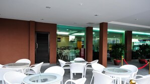 An outdoor seating area with white wicker chairs and tables, glass partitions, and potted plants. - Hallmark View Hotel (Malacca City)