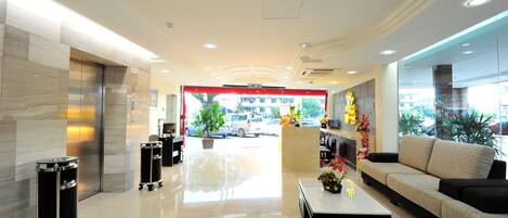 A modern hotel lobby with a reception desk, seating area, and a view of the street outside.