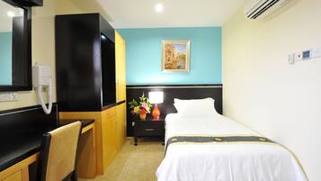 A hotel room with a bed, a desk, a chair, a nightstand with a lamp, and a painting on the wall.