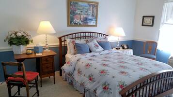 A neatly arranged bedroom with a bed, bedside tables, a chair, a desk, and a painting on the wall.