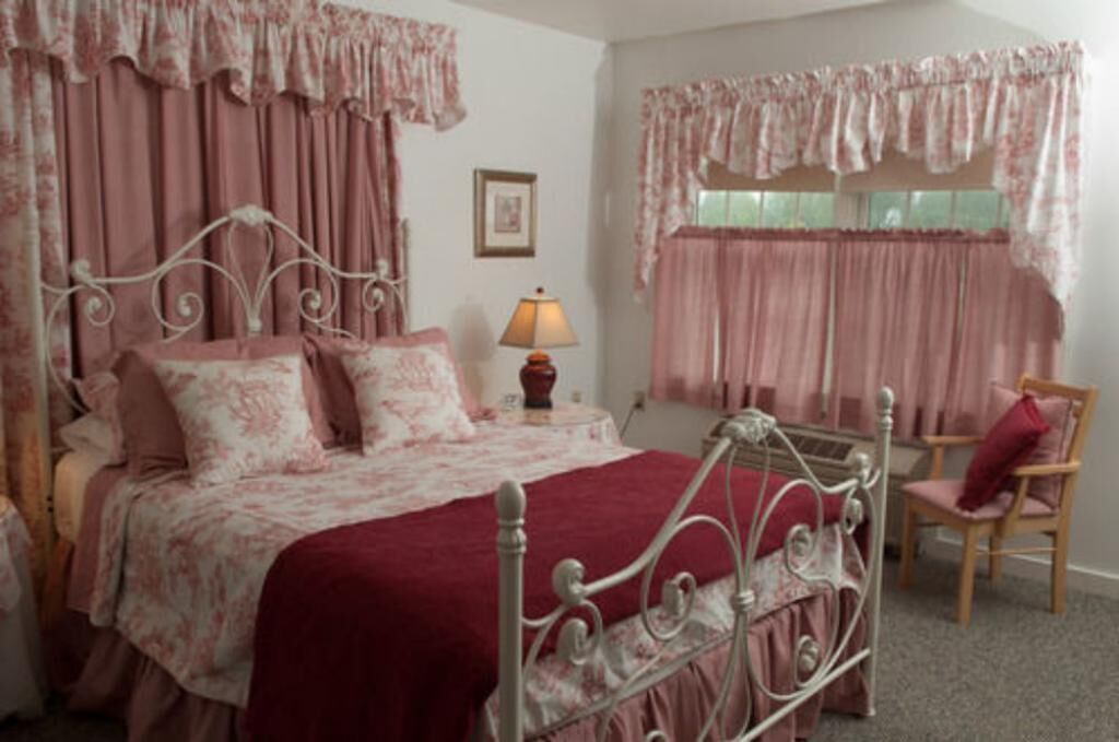 A bedroom with a metal bed frame, a red bedspread, and matching curtains.
