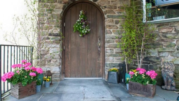 A stone building with a wooden door, a wrought iron gate, and potted plants. - Camelot Restaurant & Inn (Clarks Summit)