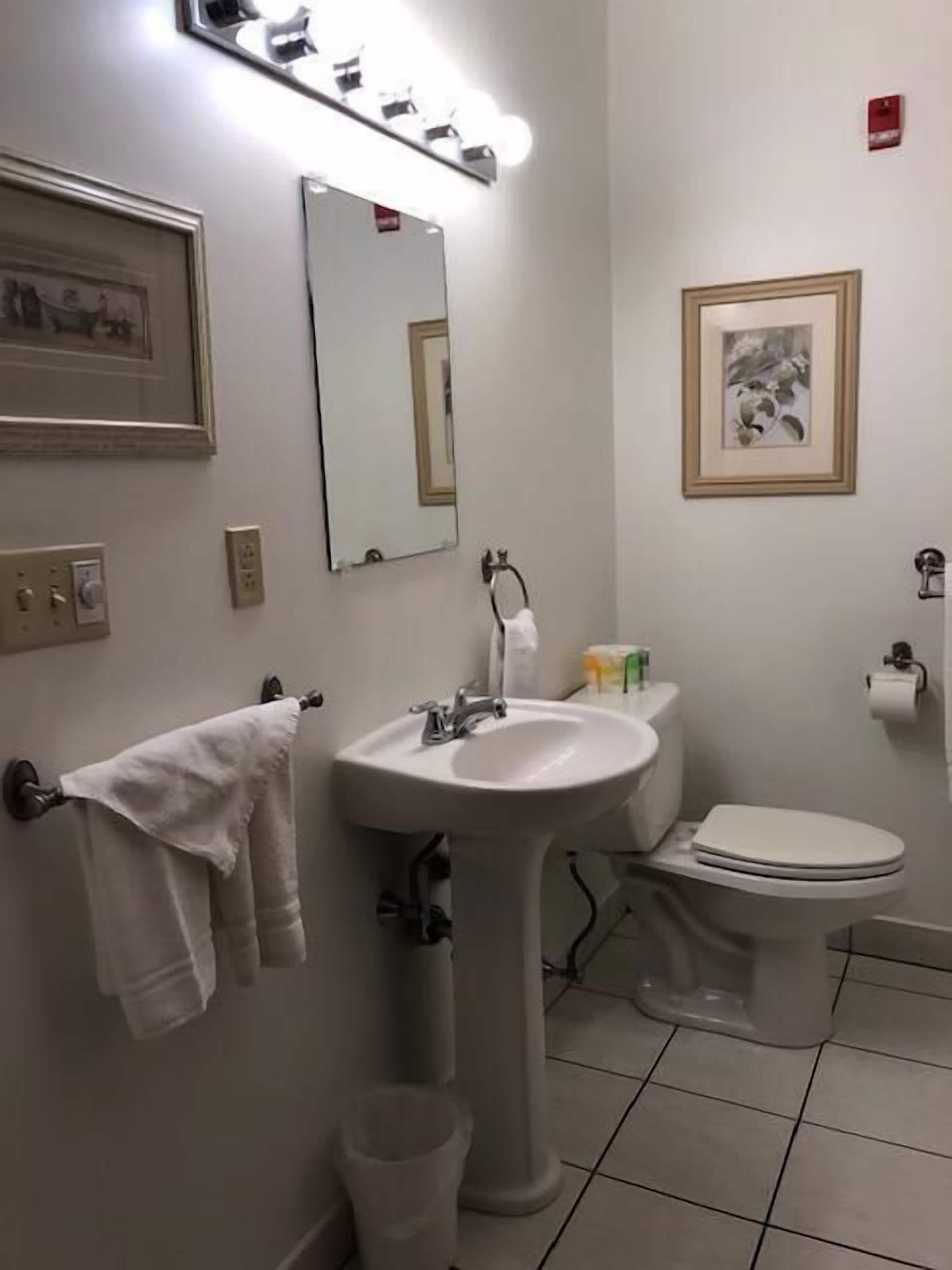 A bathroom with a sink, mirror, toilet, and framed pictures on the walls.