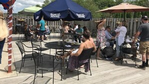 An outdoor patio with round tables and chairs, umbrellas, and a wooden fence in the background. - Camelot Restaurant & Inn (Clarks Summit)