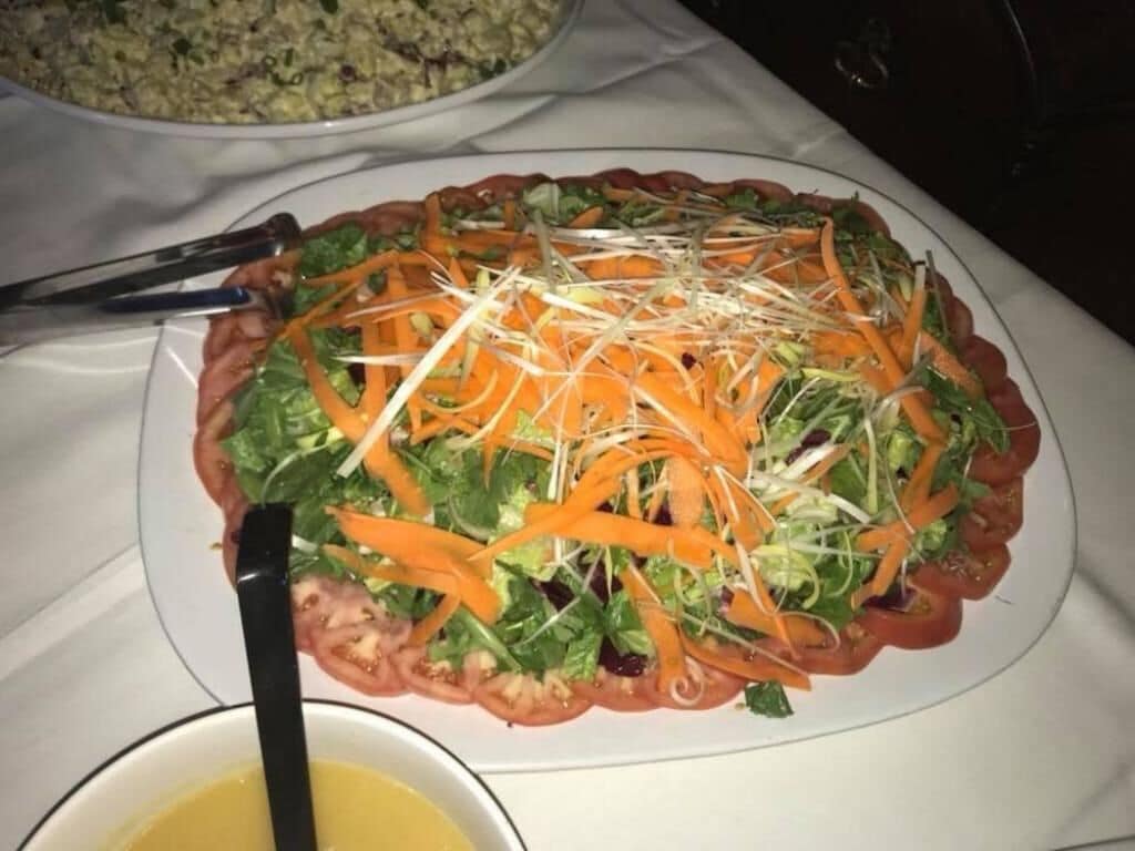 A salad on a plate with a black spoon beside it.