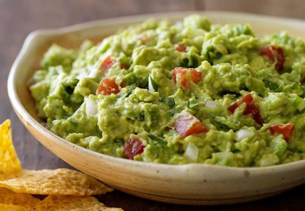 Un tazón de guacamole con trozos de tomate y cebolla.