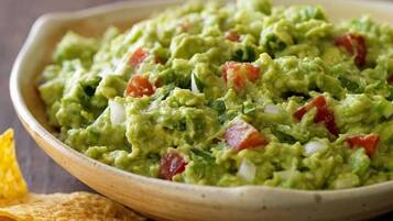 Un tazón de guacamole con trozos de tomate y cebolla.