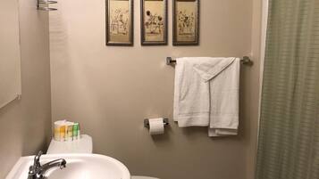 Een badkamer met een wastafel, toilet en douchegordijn. Er hangen drie ingelijste foto’s aan de muur, een handdoekhouder met een handdoek en toiletpapier.