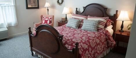 A neatly made bed with a wooden headboard, two bedside tables with lamps, a framed picture on the wall, and a window with curtains.