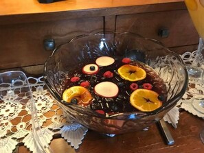A glass bowl filled with a dark liquid, containing slices of apple, orange, and berries.