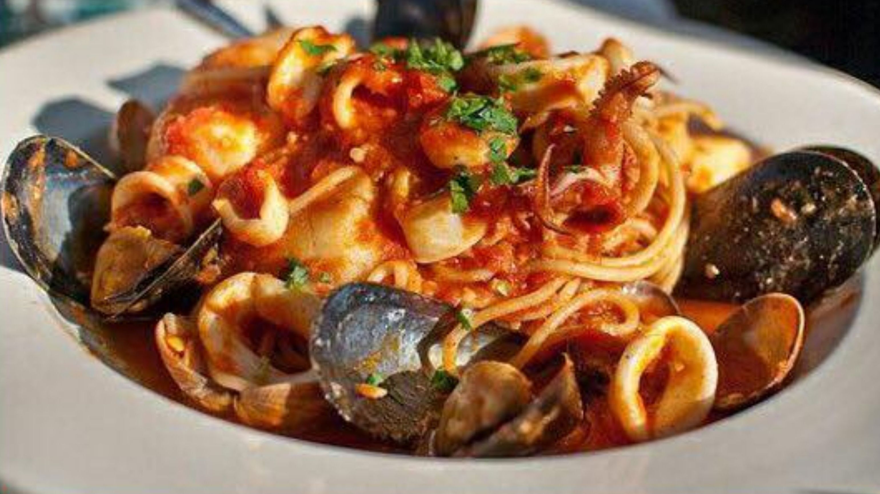 A plate of pasta with clams and a tomato-based sauce, garnished with herbs.