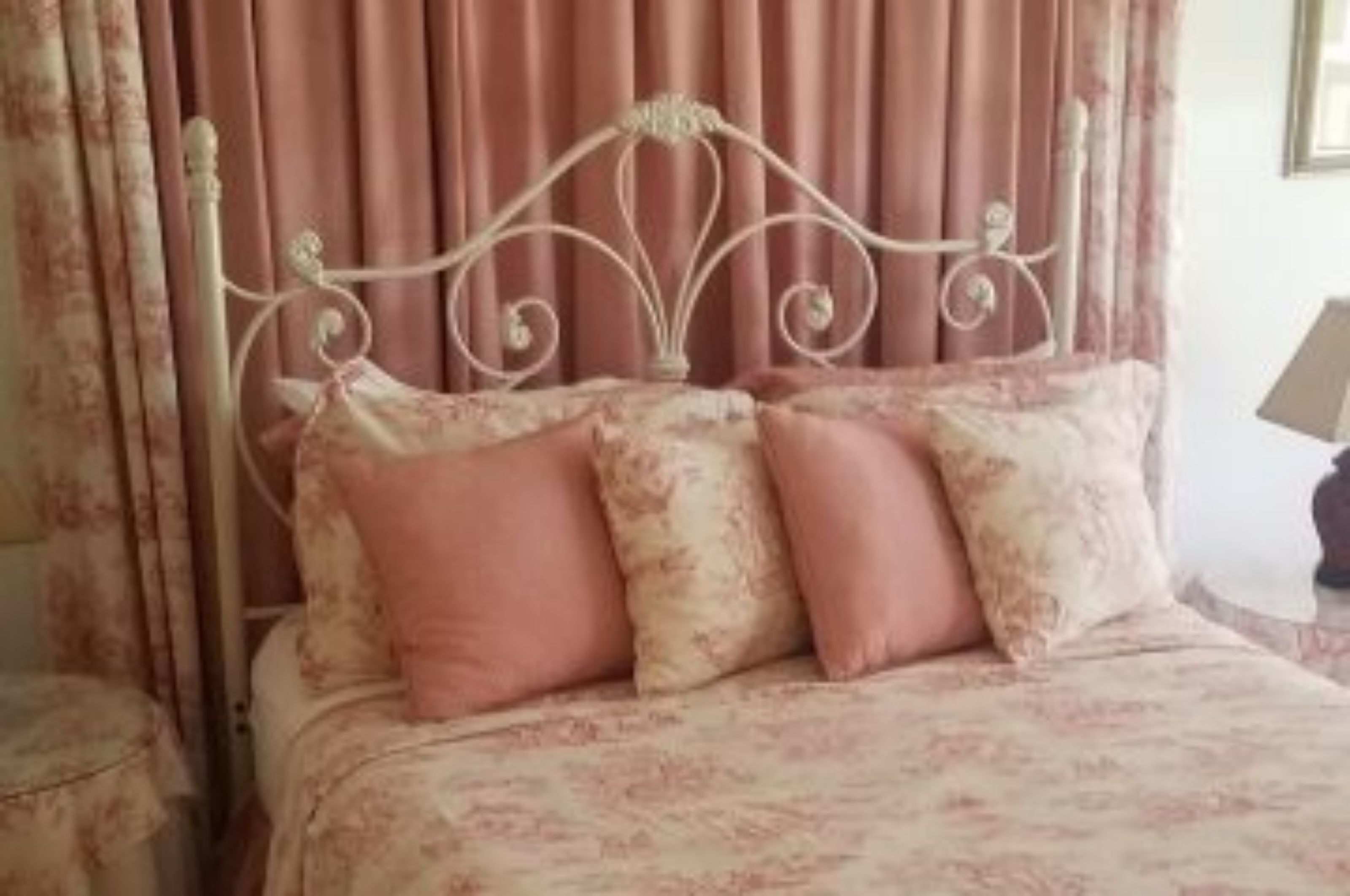A bed with a metal headboard, pink floral bedding, and matching pillows.