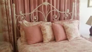 A bed with a metal headboard, pink floral bedding, and matching pillows.