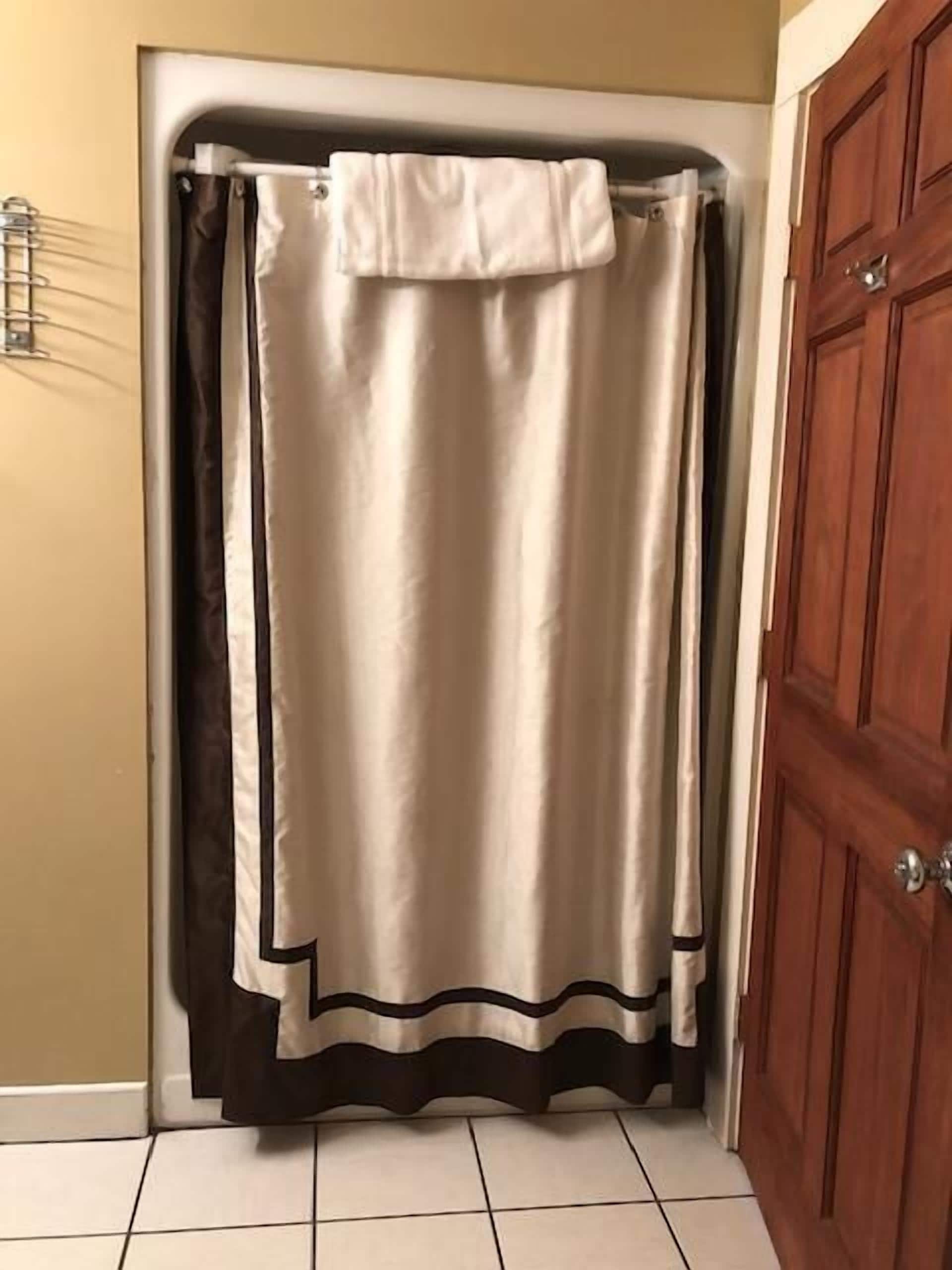 A bathroom with a shower curtain, a wooden door, and tiled flooring.