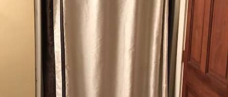 A bathroom with a shower curtain, a wooden door, and tiled flooring.