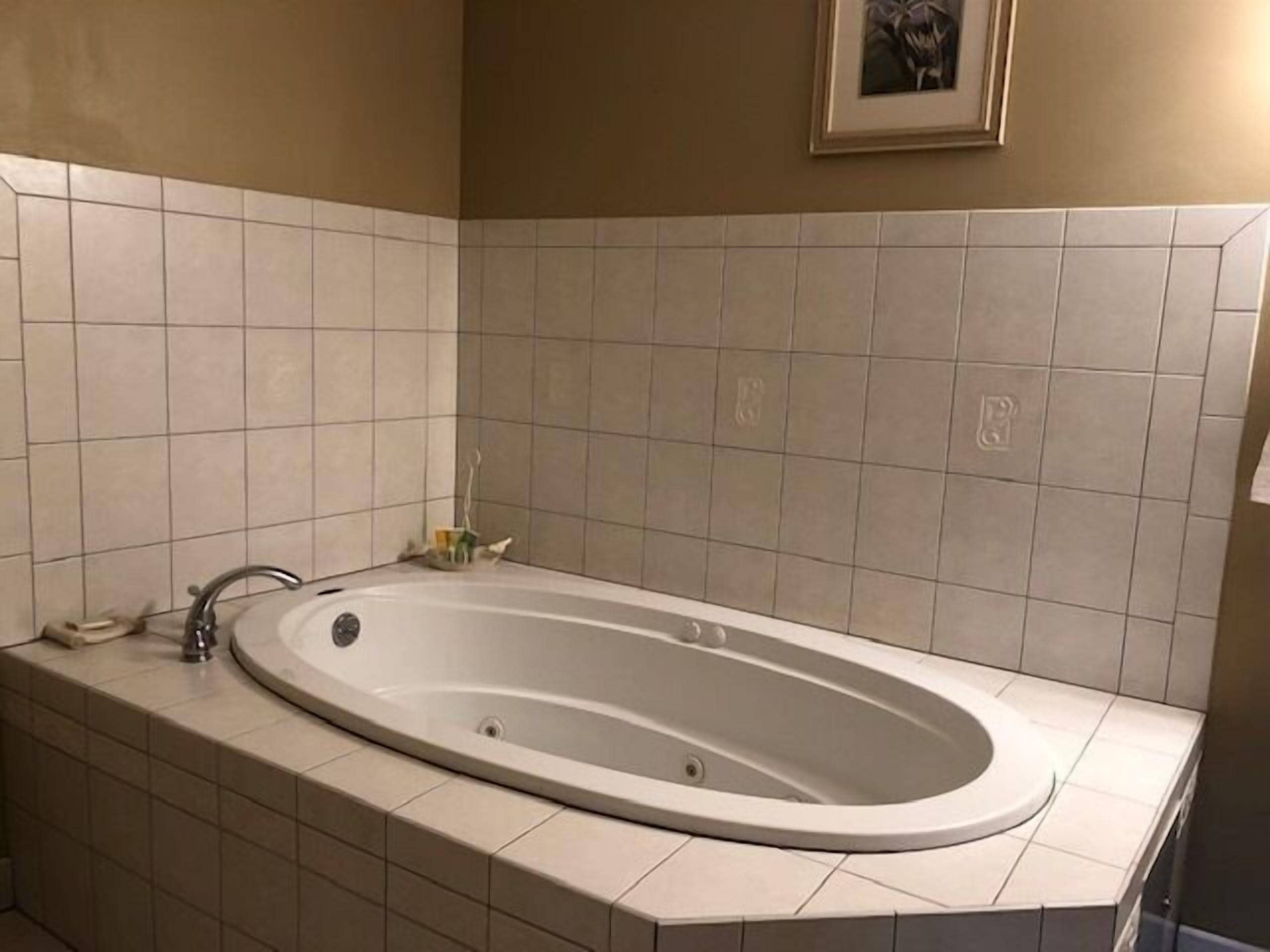 A modern bathroom with a freestanding bathtub, beige tiles, and a framed picture on the wall.