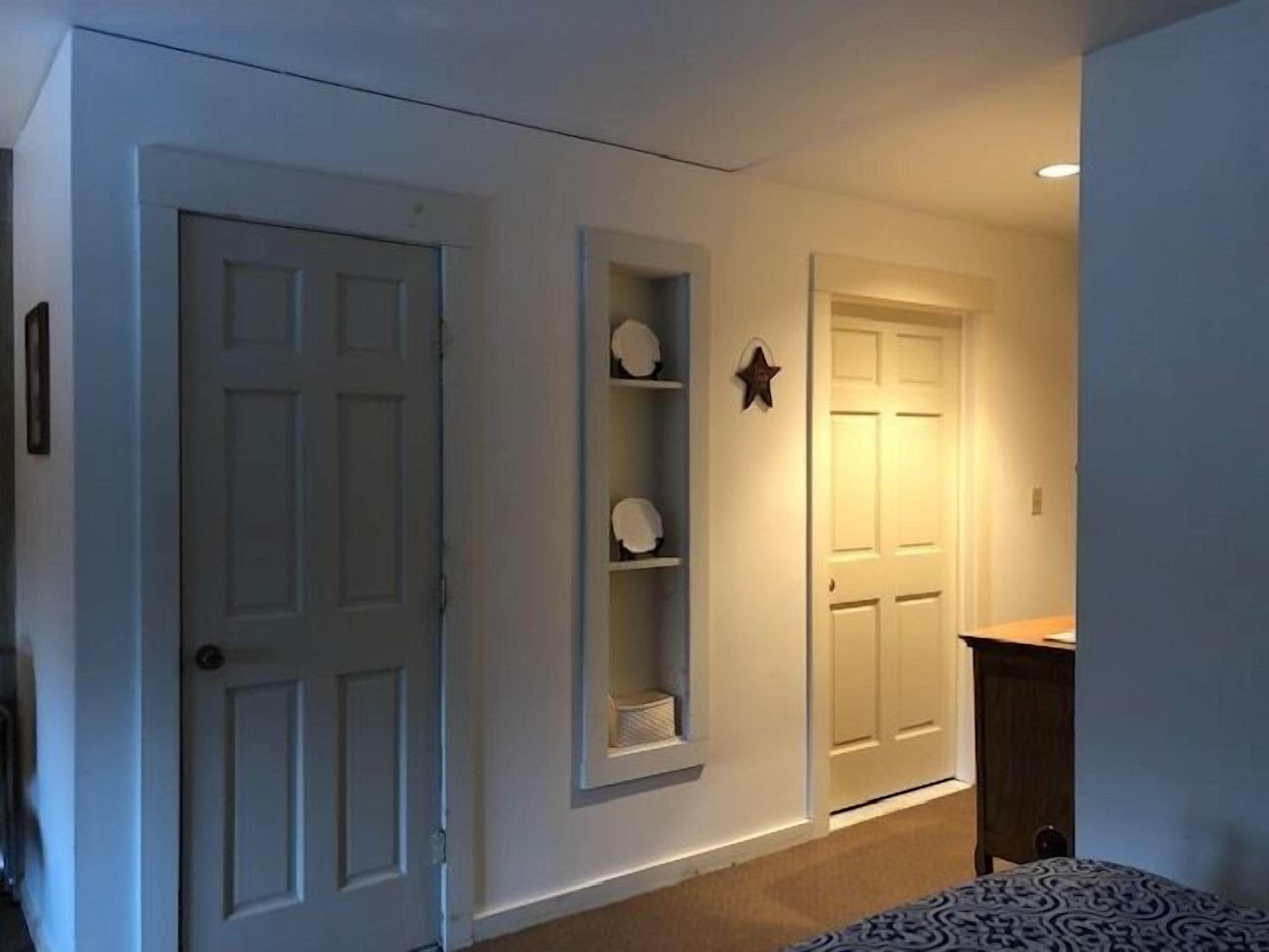 A hallway with a white door, a shelf with decorative items, and a star-shaped decoration on the wall.