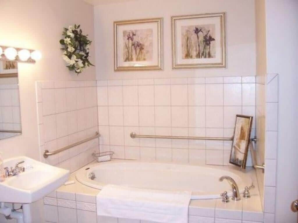 A bathroom with a bathtub, a sink, and a mirror. There are two framed pictures on the wall.