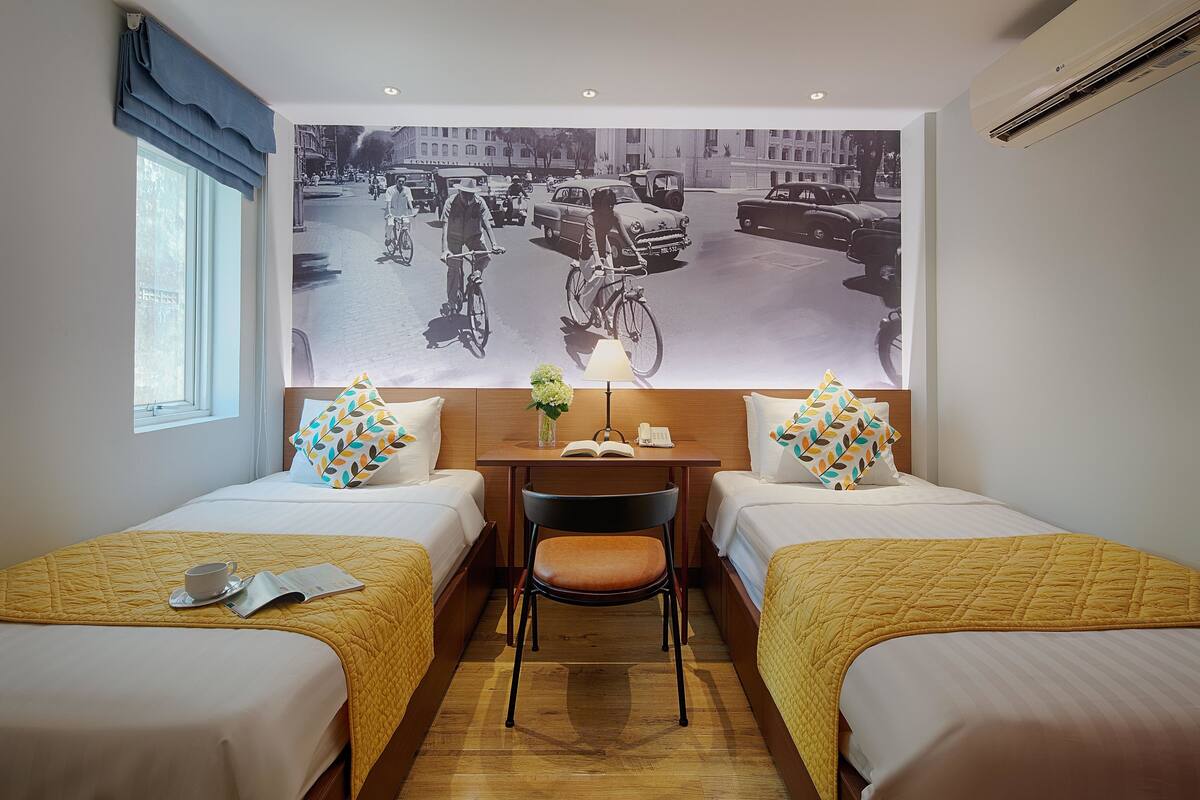 Habitación de hotel con dos camas, un escritorio y un mural grande en la pared.