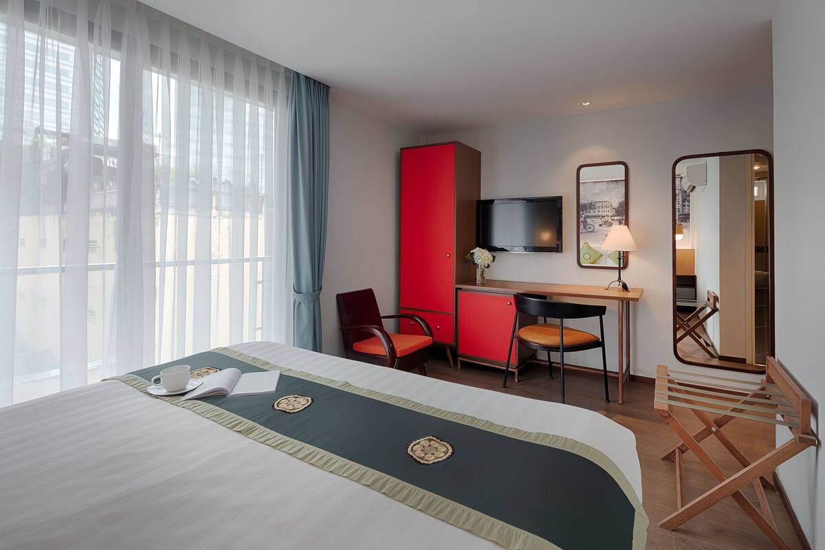 Una habitación de hotel con cama, escritorio, armario rojo, televisor y espejo.