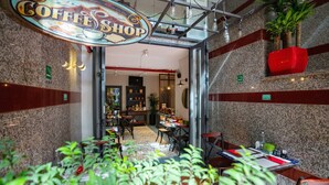 Una cafetería con un letrero sobre la entrada, mesas con sillas y plantas al frente.