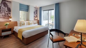 Una habitación de hotel con una cama grande, un escritorio con lámpara, una silla, una mesita de noche y una ventana con cortinas.