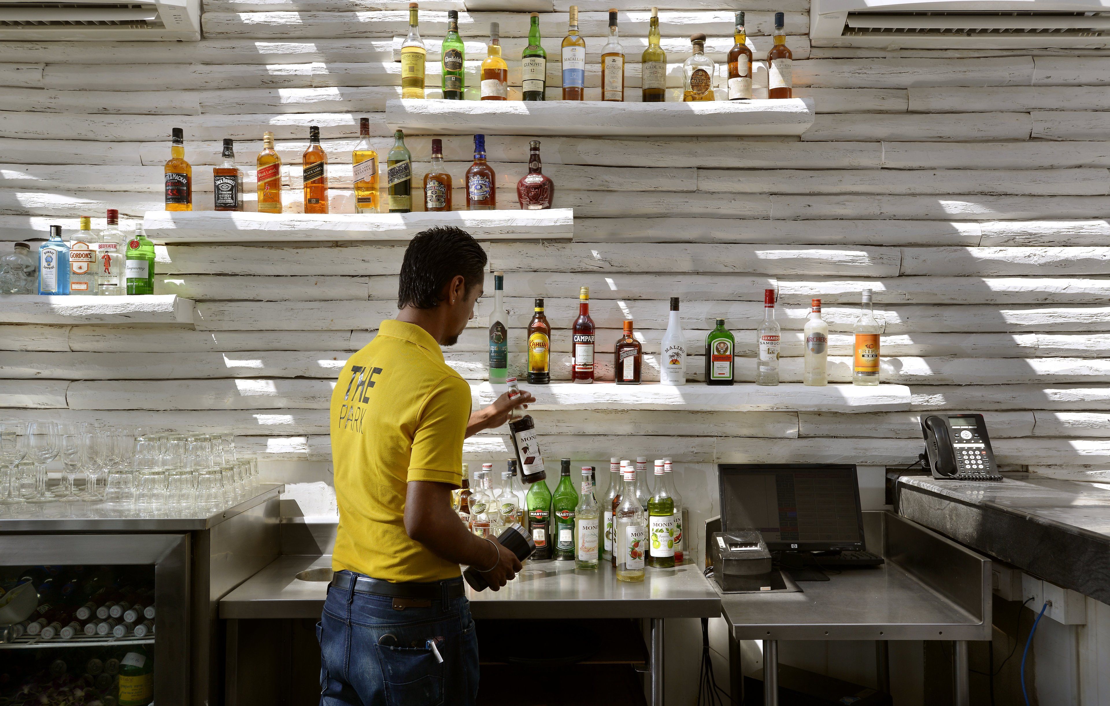 A bar area with shelves of liquor bottles, a man in a yellow shirt, and a phone on the counter.
