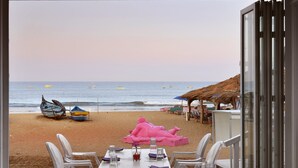 Un comedor con mesa y sillas frente a una playa con barcos y sombrillas.