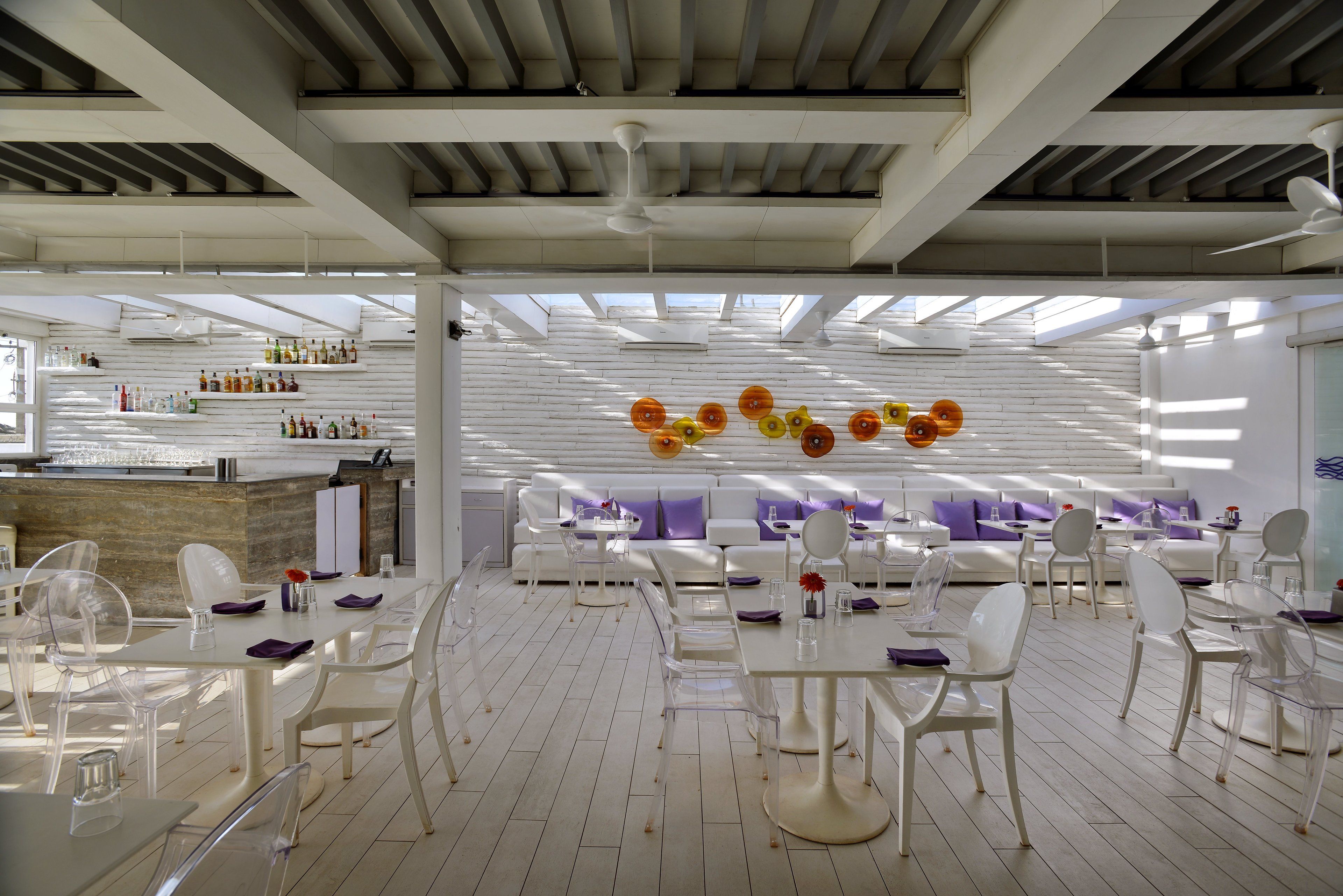 Un comedor moderno con mobiliario blanco, una barra con botellas y un techo con ventiladores.