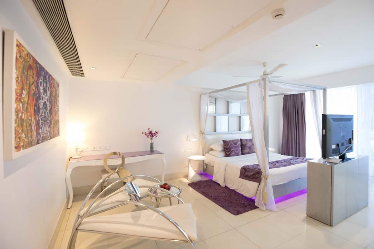 Quarto de hotel moderno com uma cama de dossel, uma escrivaninha com cadeira, televisão e uma janela grande com cortinas.
