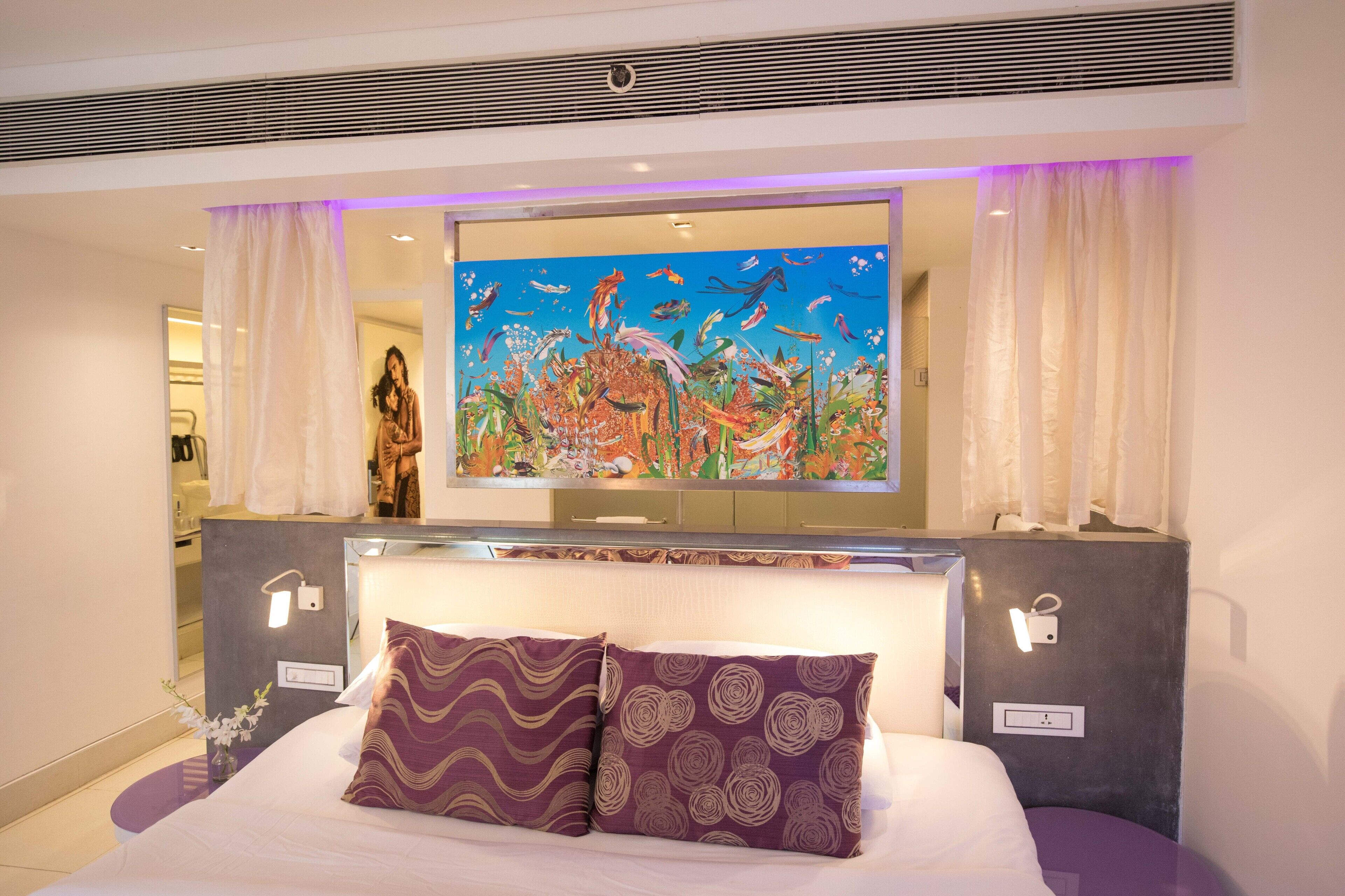 A hotel room with a large bed, two patterned pillows, a wall-mounted TV, and a mirror above the bed.
