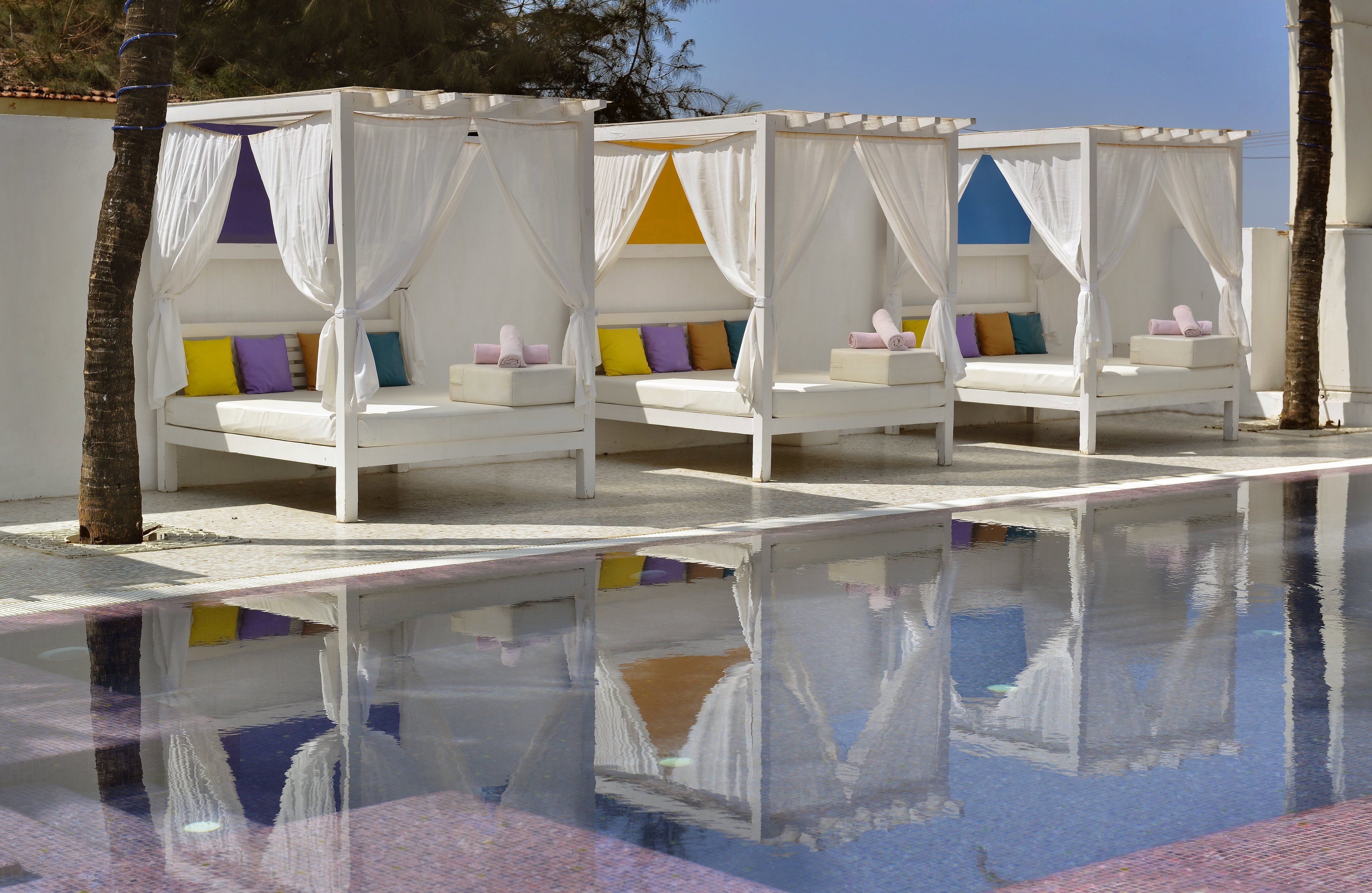 A poolside area with four white canopy beds, each with colorful pillows.